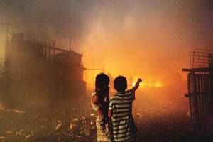Two children watch as their homes and school building burn to the ground. 